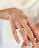 Hånd med elegant gullring og armbånd, mot lys bakgrunn. Tidløs og minimalistisk smykkestil.
