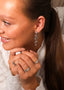 Nærbilde av en elegant kvinne med Daisy Flower øredobber i sølv med hvite cubic zirconia stener. På hendene har hun to melodie ringer i sølv, en med hvit sten og en med blå, hun har også på en star wave ring i sølv.