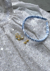 Delikate smykker og en blå hårbøyle hviler på en nydelig sølv paljett kjole.