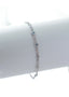 Et delikat sølvarmbånd plassert på en hvit bakgrunn. Armbåndet har små blomstrer med lysblå krystaller i midten, noen irregulære figurer som kan minnes om strandskjell, stener med hvite krystaller i midten, og en liten sol med oliven farget krystall i midten.