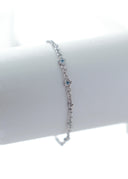 Et delikat sølvarmbånd plassert på en hvit bakgrunn. Armbåndet har små blomstrer med lysblå krystaller i midten, noen irregulære figurer som kan minnes om strandskjell, stener med hvite krystaller i midten, og en liten sol med oliven farget krystall i midten.