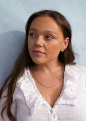 Portrett av en ung kvinne med gulløreringer og en enkel kjede, hvit bluse med rysjekant