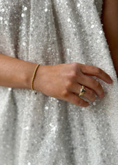 En elegant håndledd med et delikat gullarmbånd og en glitrende ring, mot en bakgrunn av en paljettkjole.