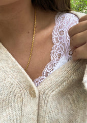 Dekorativt gullkjede anheng rundt kvinnens hals over hvit blonder topp