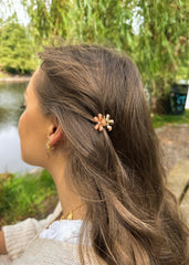 Kvinne sett fra siden med en gullblomst hårnål i brunt hår ved en innsjø