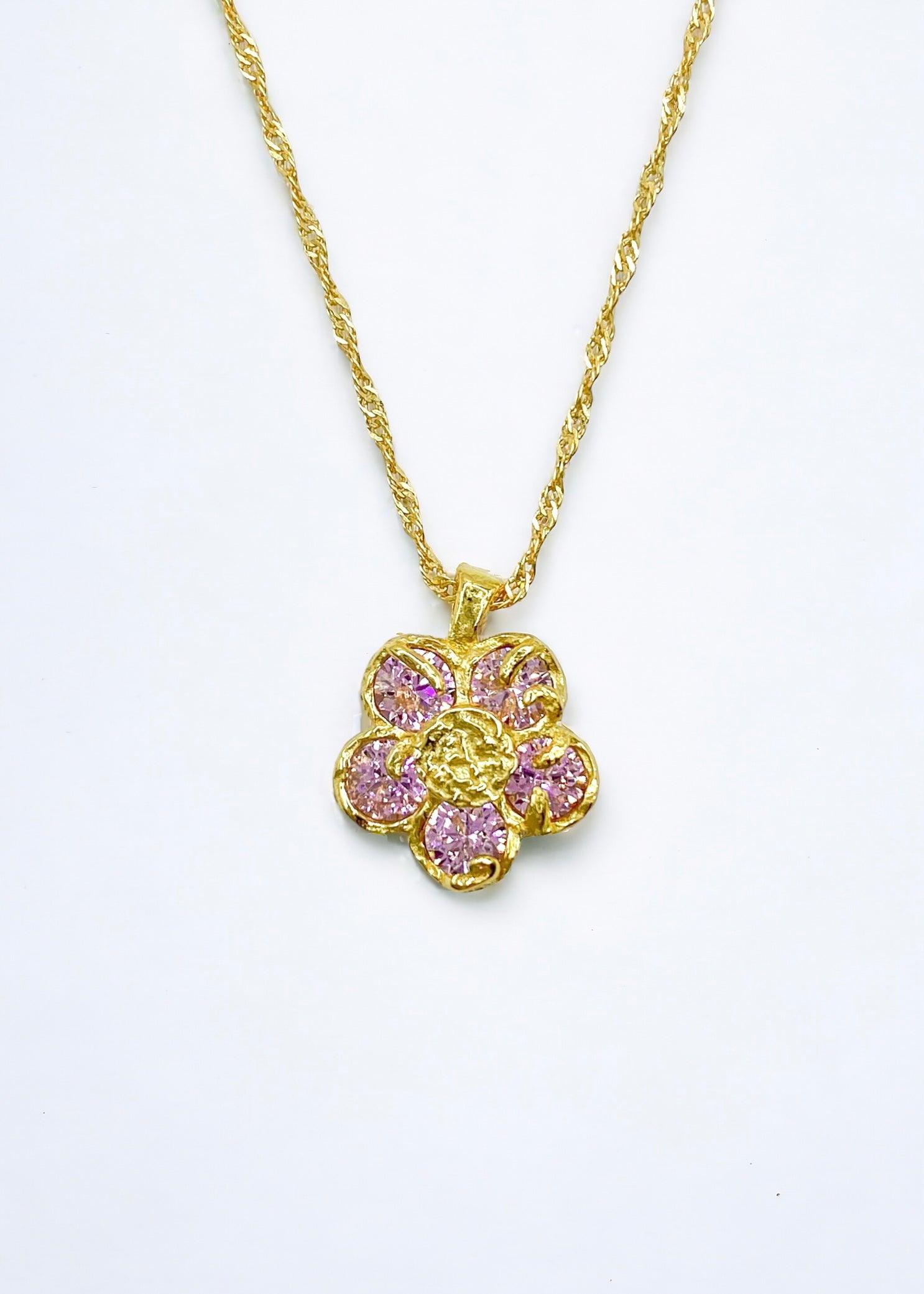 Gullblomsterkjede med rosa krystaller plassert på en elegant hvit bakgrunn.