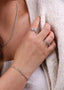 Nærbilde av håndleddet til en kvinne i ført en hvit sommerkjole og bærer et elegant sølvarmbånd. På hånden har hun to melodie sølv ringer med hvit sten og lysblå sten som matcher armbåndet.