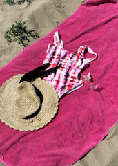 På toppen av et rosa håndkle, pent arrangert på stranden, ligger en rosa badedrakt, en gul solhatt og en hvit og rosa sommerfuglhårklype