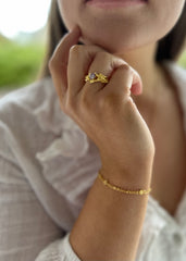 Nærbilde av en kvinne som poserer med hånden sin, i ført en gullring med lilla sten og gullarmbånd.