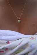 Nærbilde av en kvinne på en strand iført håndkle med Lykkesten halskjede i gull med blå cubic zirconia stein.