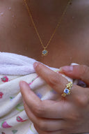 Nærbilde av en kvinne på en strand iført håndkle med Lykkesten halskjede i gull med blå cubic zirconia og matchende melodie ring i gull med blå cubic zirconia.