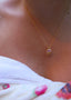 Nærbilde av en kvinne på en strand iført håndkle med Lykkesten halskjede i gull med rosa cubic zirconia stein.