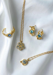 Vakker smykkekolleksjon bestående av en gull ring, halskjede formet som en sten og blomst og øredobber med blå stener farget som havet.
