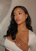 Elegant kvinne med mørkt hår og beige topp i ført matchende gull smykker med lilla stener.