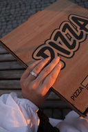 En kvinne holder hånden sin på en pizza eske. På hånden har hun en Star Wave ring i sølv. Bildet utstråler en kul vibe med blanding av elegant ring og gate stil. Bilde er tatt i golden hour, og lyset gir en fin farge på ringen.