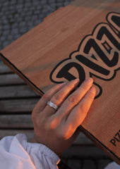 En kvinne holder hånden sin på en pizza eske. På hånden har hun en Star Wave ring i sølv. Bildet utstråler en kul vibe med blanding av elegant ring og gate stil. Bilde er tatt i golden hour, og lyset gir en fin farge på ringen.