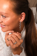 Nærbilde av en elegant kvinne med Daisy Flower øredobber i sølv med hvite cubic zirconia stener. På hendene har hun to melodie ringer i sølv, en med hvit sten og en med blå, hun har også på en star wave ring i sølv.