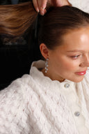 En kvinne med brunt hår holder hestehalen sin opp, i øret henger Daisy Flower øredobber i sølv med hvite stener.