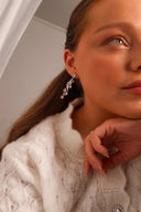 Nærbilde av en kvinne med Daisy Flower øredobber i sølv med hvite stener. Kvinnen har mørkt brunt hår og hvit strikket genser. Øredobbene ser elegante ut til antrekket.