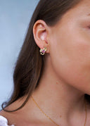 Sideprofil av kvinne med brunt hår og hvit topp med blå bakgrunn utsmykket med gulløredobb som bærer en rosa sten.