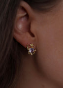 Nærbilde av en kvinne med brunt hår utsmykket med en gulløredobb med lilla sten i øret.