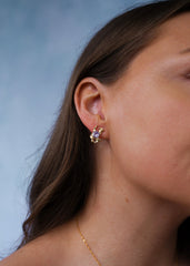 Sideprofil av en kvinne med brunt hår utsmykket med gulløredobb med lilla sten i en blå bakgrunn.