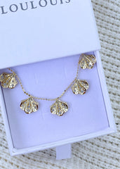 En delikat smykkeboks som inneholder et gullhalskjedet med anheng formet som kamskjell og hvite stener.