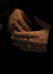 Nærbilde av kvinnes hender krysset med unike gullringer med innfelte edelstener, kontrast mot mørk bakgrunn for eksklusive smykker