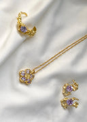 En vakker gull smykke kolleksjon bestående av ring, halskjede og øredobber med lilla stener.