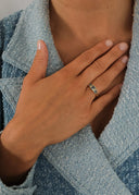 Hånd som hviler over brystet med blå steinring, iført teksturert blå jakke.