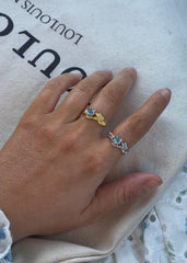 En hånd som lener seg over et bærenett i ført to ringer i gull og sølv med blå stener.