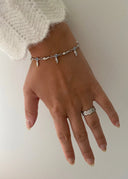 En delikat hånd foran en hvit vegg i ført sølv armbånd og ring. 