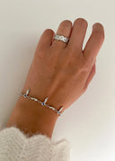 En delikat hånd foran en hvit vegg i ført sølv armbånd og ring. 