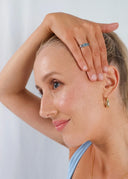 Kvinne smilende med hånden løftet mot hodet, iført en blå og en gul ring med steiner på fingrene og en gullørering, kledd i lyseblå topp.