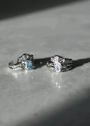 to sølv ringer med hvite og blå stener på en marmor flate lyst opp av en stråle med sol. 