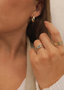 Nærbilde av kathrina ringen, starwave ringen og dome hoops i gull. Kvinnen holder hånden elegant inntil øret slik at smykkene er i sentrum.