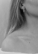Nærbilde av øret til en kvinne. Bilde er tatt i sort/hvitt. I øret henger en delikat øredobb, Dome hoops i sølv.