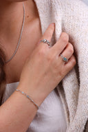 Nærbilde av håndleddet til en kvinne i ført en hvit sommerkjole og bærer et elegant sølvarmbånd. På hånden har hun to melodie sølv ringer med hvit sten og lysblå sten som matcher armbåndet.