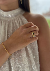 Stilfull kvinne med gullarmbånd og detaljert ring, halvprofil, foran en glitrende sølvkjole for festtilbehør