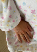 Bilde av en hånd med melodie ring i rosa. Hånden lener seg inntil en blomstrete badekåpe.