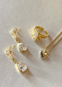 Gullfargede øredober, en ring og et halskjede på en hvit flate. 