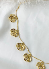Elegant gullsmykke med kamskjell anheng som bærer hvite stener på en hvit bakgrunn.