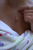 Nærbilde av en kvinne på en strand iført håndkle med Lykkesten halskjede i gull med lavendel cubic zirconia og matchende melodie ring i gull med lavendel cubic zirconia.