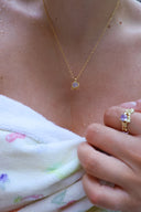 Nærbilde av en kvinne på en strand iført håndkle med Lykkesten halskjede i gull med lavendel cubic zirconia og matchende melodie ring i gull med lavendel cubic zirconia.