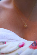 Nærbilde av en kvinne på en strand iført håndkle med Lykkesten halskjede i gull med rosa cubic zirconia stein.