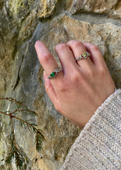 En kvinne som holder hånden sin over natur stener, i ført en strikket genser og to vakre sølvringer med smaragd og oliven fargede stener.