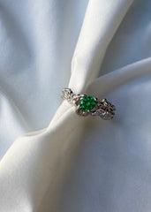 Sølv ring med smaragd sten tullet inn i elegant hvitt silkestoff.