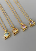 Fire gullhalskjeder plassert på en grålig bakgrunn for å fremheve de vakre fargene stenene bærer.