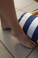 En kvinne fot lener seg inntil en sommerlig pute, på foten har hun Sunflower Anklet i gull. Smykket gir en elegant og delikat utstråling.