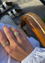 En kvinnehånd lener seg på en hvit kjole. På hånden har hun en Luna ring i gull med vakre lavendel fargede zirconia stener, og en Star Wave ring i gull.